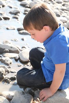 Younb boy sitting outside on pebble beach