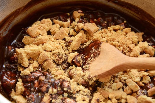 Stirring crushed digestive biscuits into melted chocolate with a wooden spoon to make rocky road