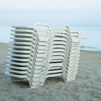Pile of white lounging chairs at dawn on the beach