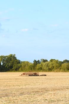 Harrow left among the stubble in a harvested farm field. Copy space above in the blue summer sky.