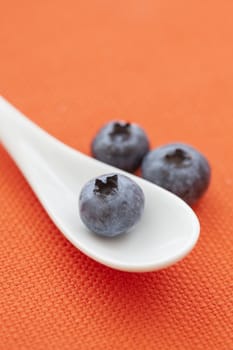 White spoon with blackberries, orange background.