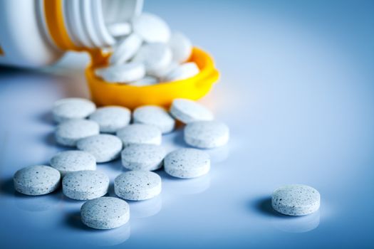 Pills spilling out of pill bottle on blue background