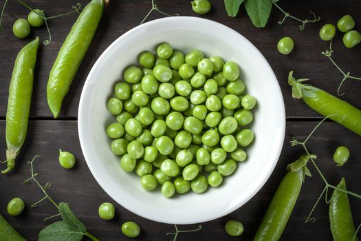 Green peas in bowl on wooden table background. Top view