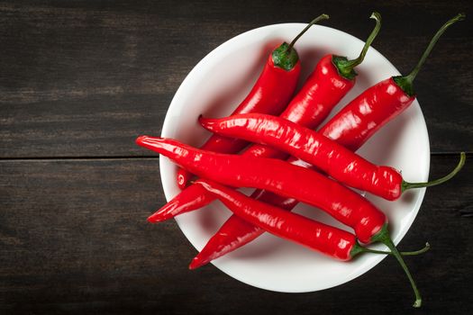 Red chili peppers on white plate on wooden table background. Copy space. Top view