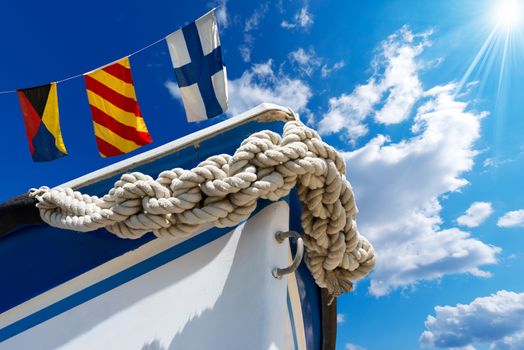 Bow of the boat adorned with knotted rope on blue sky with three nautical flags and space for text