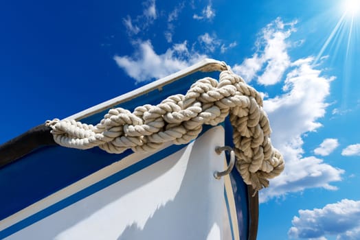 Bow of the boat adorned with knotted rope on blue sky with sun rays and space for text