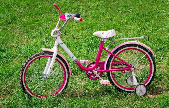 The beautiful bicycle bright pink color for the girl. Is on a lawn with a green grass.
