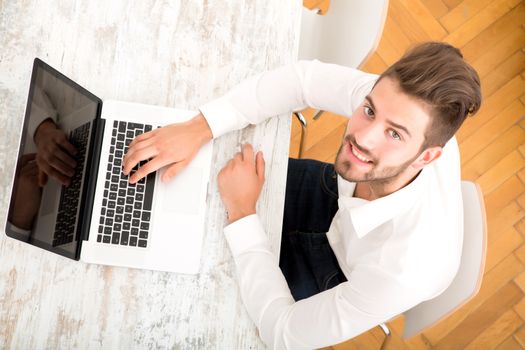 A young man sitting at the table with a laptop computer.