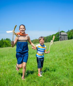 Cute kids runing on grass in summer day holds wooden windmill in hand