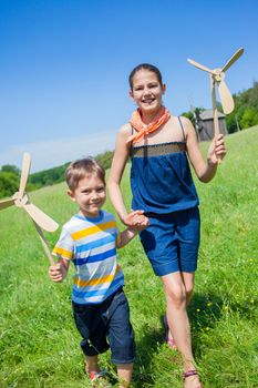 Cute kids runing on grass in summer day holds wooden windmill in hand