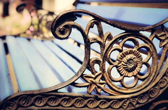 Detail of old park bench with ornaments and bokeh background, filtered vintage style