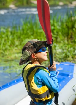 Portrait of happy young boy holding paddle near a kayak on the river, enjoying a lovely summer day