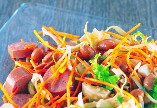 Salad with sausage, cheese, carrots, beans over glass plate