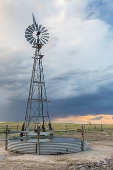 windmill with a pump and cattle water tank in shortgrass prairie against stormy sky, iPawnee National Grassland in Colorado near Grover