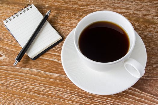 White cup of coffee on wooden table with notebook