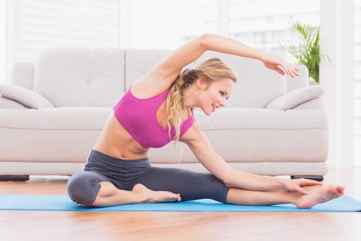 Fit blonde stretching on exercise mat at home in the living room