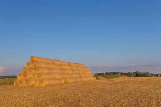 Piled hay bales on a field against blue sky at sunset time