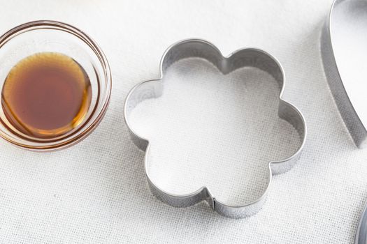 Flower shaped cookie cutter and small glass bowl of vanilla extract.