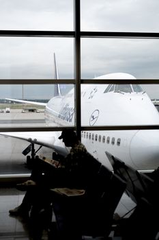 FRANKFURT, GERMANY - JULY 21: Silhouette of passenger waiting for flight in terminal with Lufthansa jumbo jet in perspective in the background.. July 21, 2014 in Frankfurt.