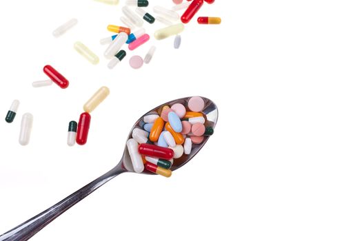 A lot of colored pills and tabs with a spoon over a white background