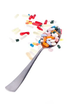 A lot of colored pills and tabs with a spoon over a white background