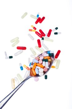 A lot of colored pills and tabs with a spoon over a white background