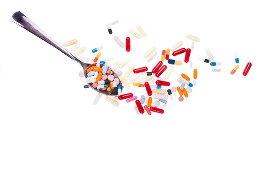 A lot of colored pills and tabs with a spoon over a white background