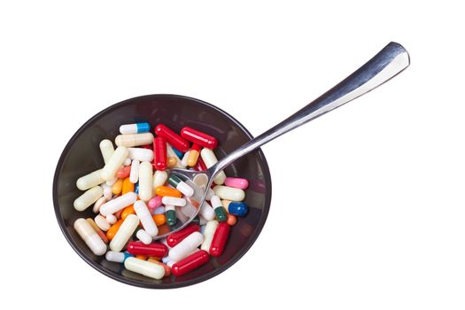 Many colored pills and capsules in a bowl with a spoon