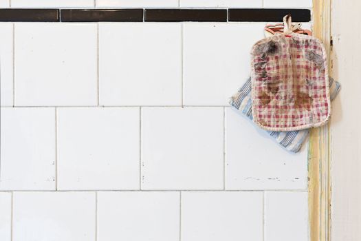 Two Old Oven Mitts on a dirty whiter tiled kitchen wall. Lot of Copy Space