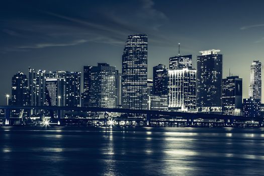 Miami city skyline panorama at dusk with urban skyscrapers and bridge over sea with reflection 