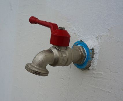 The old style of faucet is made of steel, with red handles, mounted on the wall.                              