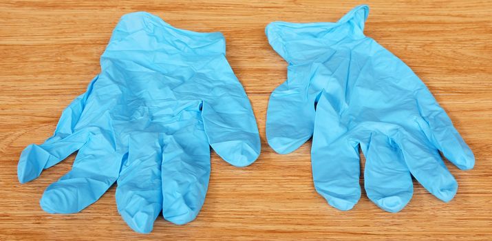 A pair of blue medical gloves, placed on the brown wood.                              