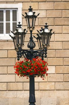 Red geraniums on a typical lamp post of Barcelona, Spain. In the background the Palau de la Generalitat de Catalunya (XV-XVII century)