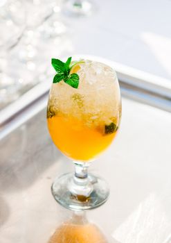 Glass of orange drink with mint leaf on silver plate
