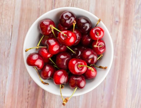 White bowl of sweet cherries on wood texture