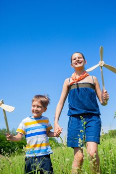 Cute kids runing on grass in summer day holds wooden windmill in hand