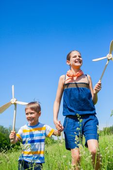 Cute kids runing on grass in summer day holds wooden windmill in hand