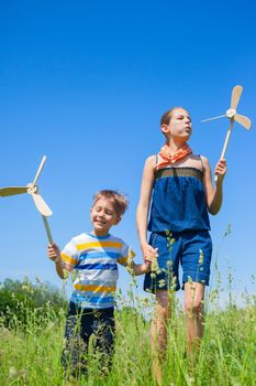 Cute kids runing on grass in summer day holds wooden windmill in hand