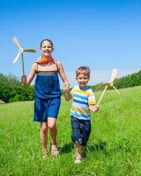 Cute kids runing on grass in summer day holds wooden windmill in hand