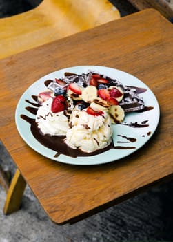 Chocolate waffles with ice cream, banana, strawberry and blueberry on wooden table