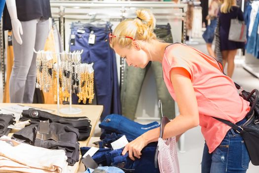 Woman shopping clothes. Shopper looking at clothing indoors in store. Beautiful blonde caucasian female model. 