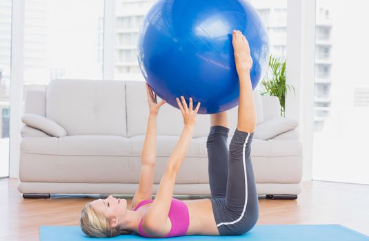 Cheerful fit blonde holding exercise ball between legs at home in the living room