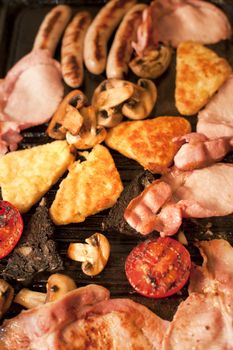Cooking breakfast for a family with a closeup overhead view of bacon, hash browns, sausages, tomato and mushrooms sizzling on a hot griddle
