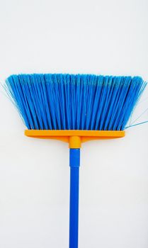 Plastic blue broom , handle is blue, placed against the white wall of house.                              