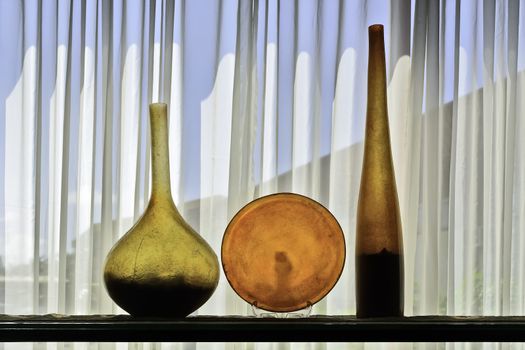 Colorful architectural bottle and plate display shot against white, translucent curtain