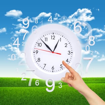 Finger points to clock face with figures on background of green grass and blue sky