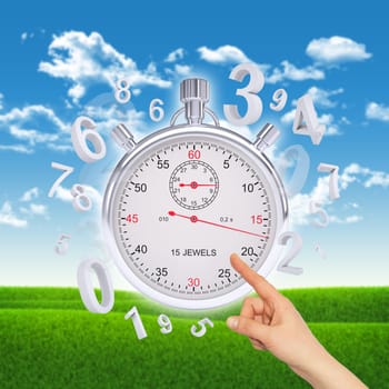 Finger points to stopwatch with figures on background of green grass and blue sky