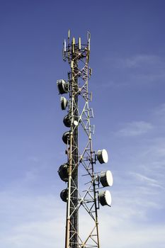 Two communication towers shot against blue sky.