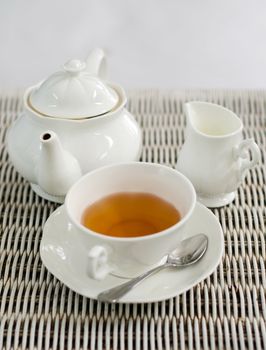 Cup of tea with little milk jar and teapot on weave texture background