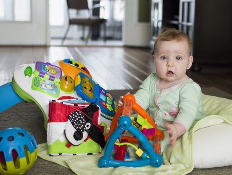 Baby sitting on floor with colorful toys looking at viewer